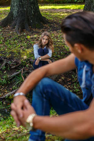Guy looking on woman who sitting on grass in the park.の写真素材