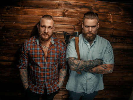 Two serious mans with beards and tattoos posing over wooden wall.の写真素材