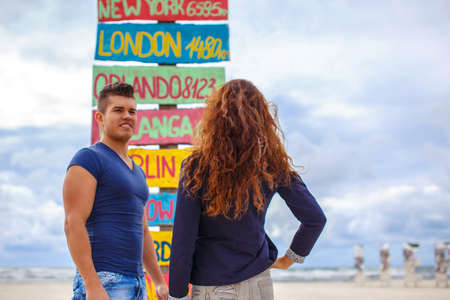 Redhead woman and sporty guy posing over singnpost with city directions.の写真素材