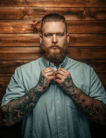 Brutal man with beard and tatoos possing over wooden wall.の写真素材