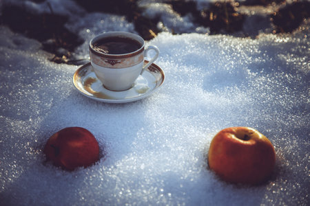 Cup of tea and apples on snow.