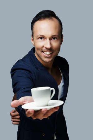 Smiling man in a suit holds white coffee cup. Isolated on grey background.の写真素材