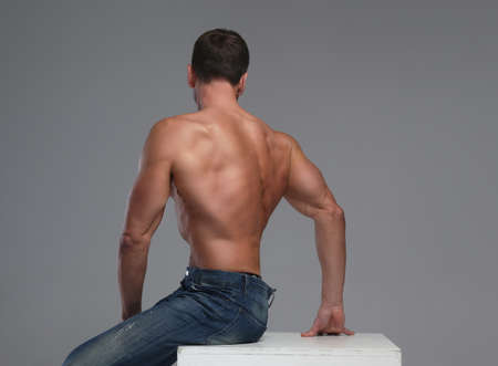Back of shirtless male in jeans over grey background.