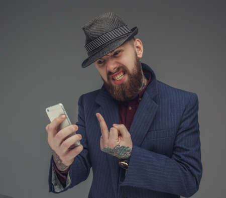 Bearded man in blue jacket looking at smartphone. Isolated on grey background.の写真素材