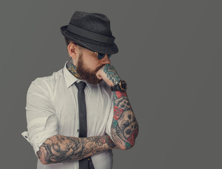 Man with tattooed arms thinking. Isolated on grey background.