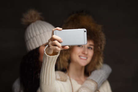 Two woman in winter hats and sweaters taking selfie with smartphone.の写真素材