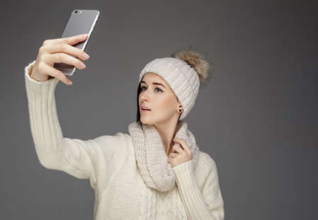 A woman in winter clothes taking pictures on smartphone.の写真素材