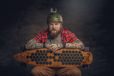 Bearded tattooed man in red shirt holding long board.