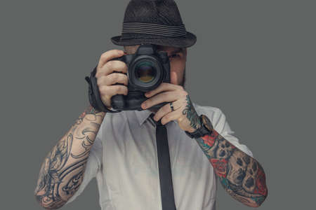 A man with tattooes on arms holding dslr photo camera. Isolated on grey background.の写真素材