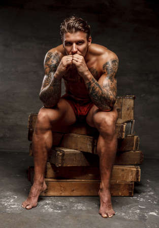 Naked muscular tattooed guy sitting on wooden boxes.の写真素材