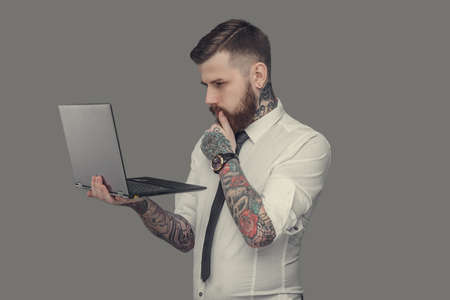 Bearded man in white shirt holding laptop. Isolated on grey background.の写真素材