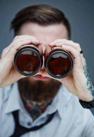 Bearded hipster man holding beer bottles like binocular.の写真素材