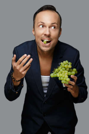 A man in blue suit holding green grape. Isolated on grey background.