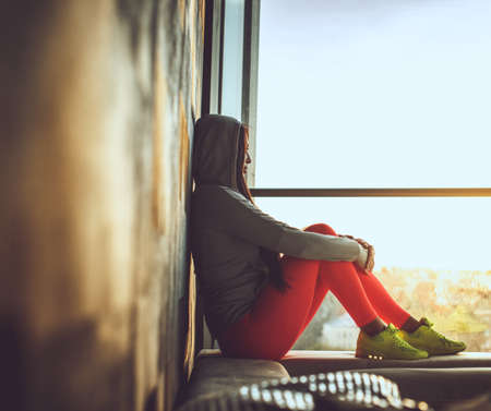 Female in red pants and yellow shoes sitting near window.の写真素材