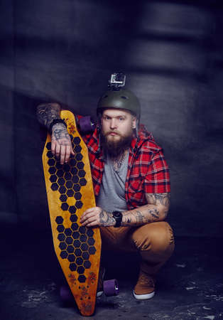Bearded tattooed man in red shirt holding long board.の写真素材