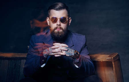 Serious bearded man in sunglasses over dark grey background.の写真素材