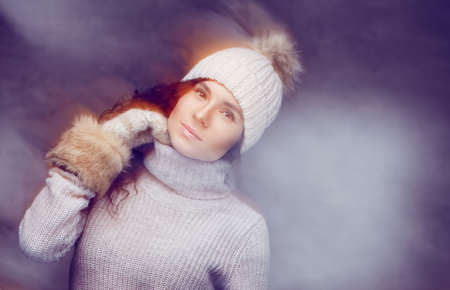 A woman in warm winter clothes holding arms in gloves near her head.
