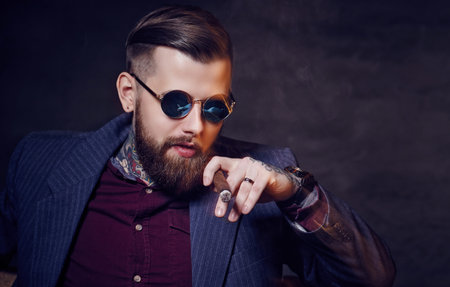 Bearded man in sunglasses smoking a cigar.の写真素材