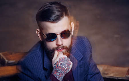 Artistic portrait of bearded man in sunglasses and with tattooes on arms.の写真素材