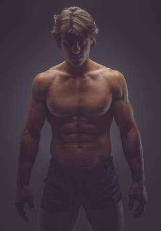 Shirtless muscular man in shorts posing in a deep shadows.の写真素材