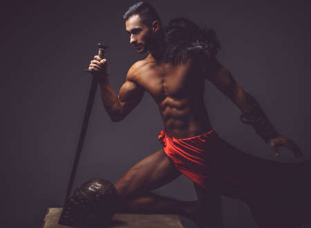Muscular man ancient Rome soldier holding a sword dressed in a red fluttering dress.の写真素材