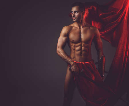 Muscular man ancient Rome soldier holding a sword dressed in a red fluttering dress.の写真素材
