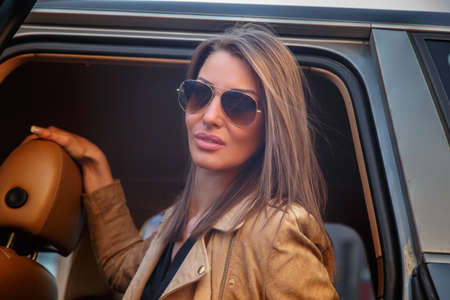 Casual young woman in sunglasses sits on a car's back seat.の写真素材
