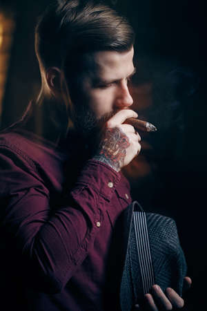 A man with tattoo on his arm smoking a cigar.