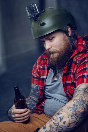 Bearded tattooed man in a red shirt posing with a longboard.の写真素材
