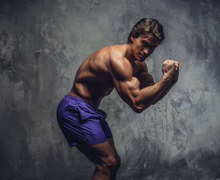Shirtless muscular man in a blue shorts posing against a grey wall.の写真素材