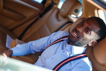 Blackman in a blue shirt sits on car's back seat.の写真素材