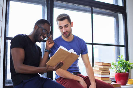 Smiling african american man with casual friend reading a book.の写真素材