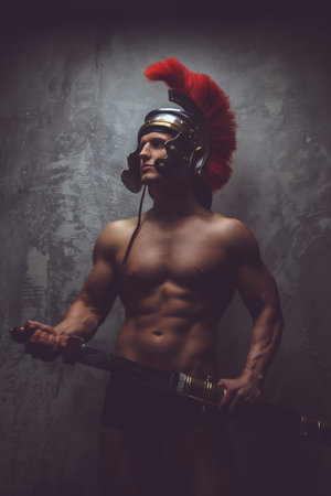 Shirtless muscular man in roman armour holds sword.