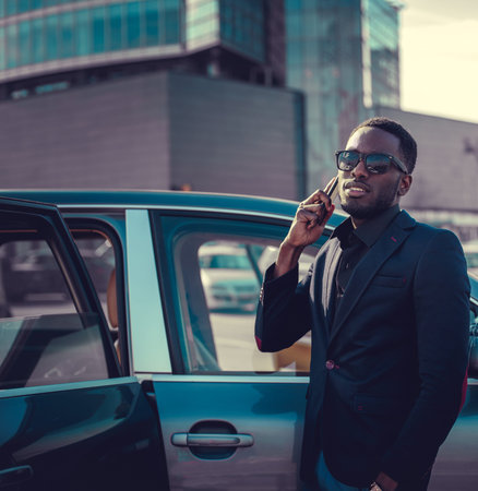 Black man in sunglasses talking by smartphone near the car.の写真素材