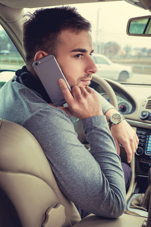 Modern man talking by smartphone in the car.