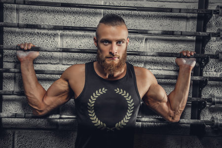 Bearded muscular man in a grey t shirt posing in a gym club.