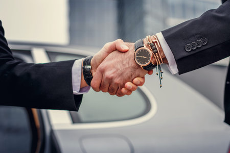 Two men handshake in front of the car.