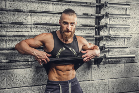 Bearded muscular man in a grey t shirt posing in a gym club.
