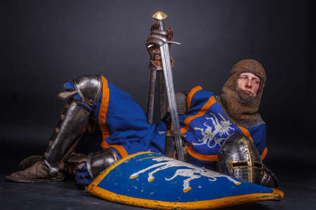 A man in kinight armour with sword isolated on a dark grey background.の写真素材