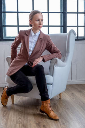 Casual young woman in a brown jacket relaxing in a room with wondow.の写真素材