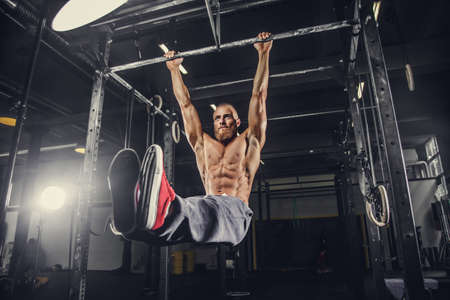 Shirtless bearded man doing stomach exercises on a horizontal bar.の写真素材