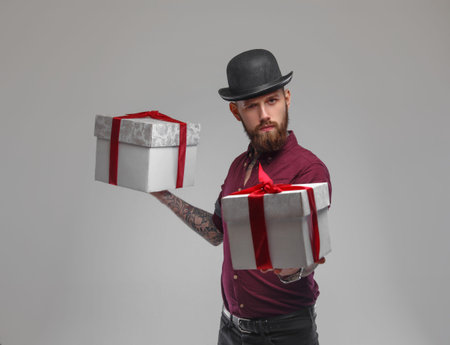 Bearded tattooed male with gift boxes isolated on a grey background.の写真素材