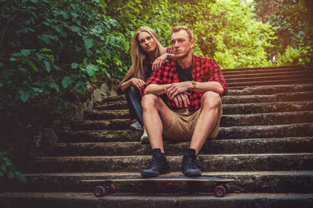 Casual moder young skateboarders couple posing on footway in a forest park.の写真素材
