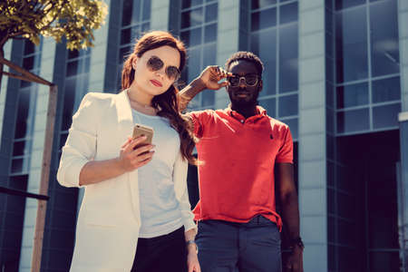 Caucasian female looking at smartphone with afro american male on a street.の写真素材