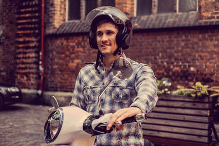 Male in a helmet on white moto scooter in old town.の写真素材