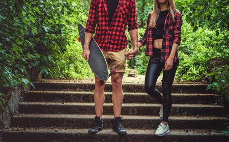 Casual moder young skateboarders couple posing on footway in a forest park.