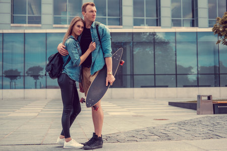 Casual couple with longboard posing on a square in a city.の写真素材