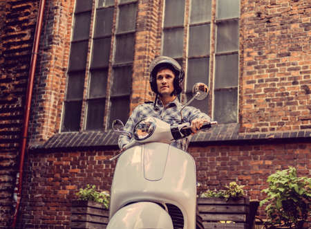 Male in a helmet on white moto scooter in old town.の写真素材