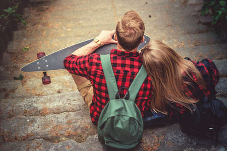 Male in a red shirt with longboard relaxing with his girlfriend on stairway in a park.の写真素材