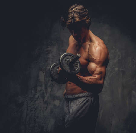 Studio portrait of sporty shirtless male with dumbbell on grey background.の写真素材